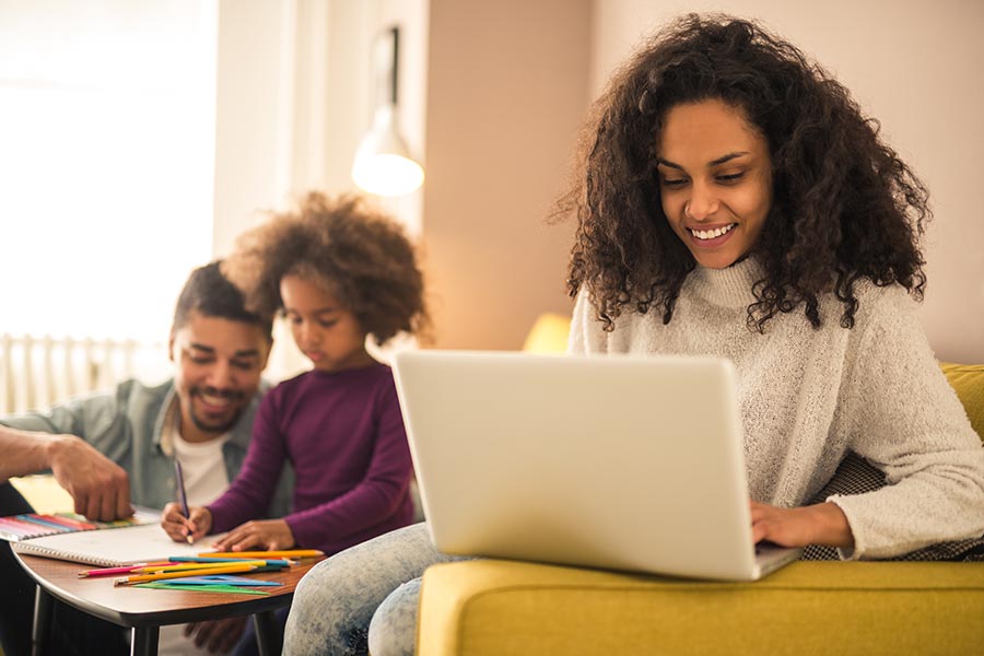 Blog - Smiling Mother Uses a Computer as Her Husband and Child Play in the Background