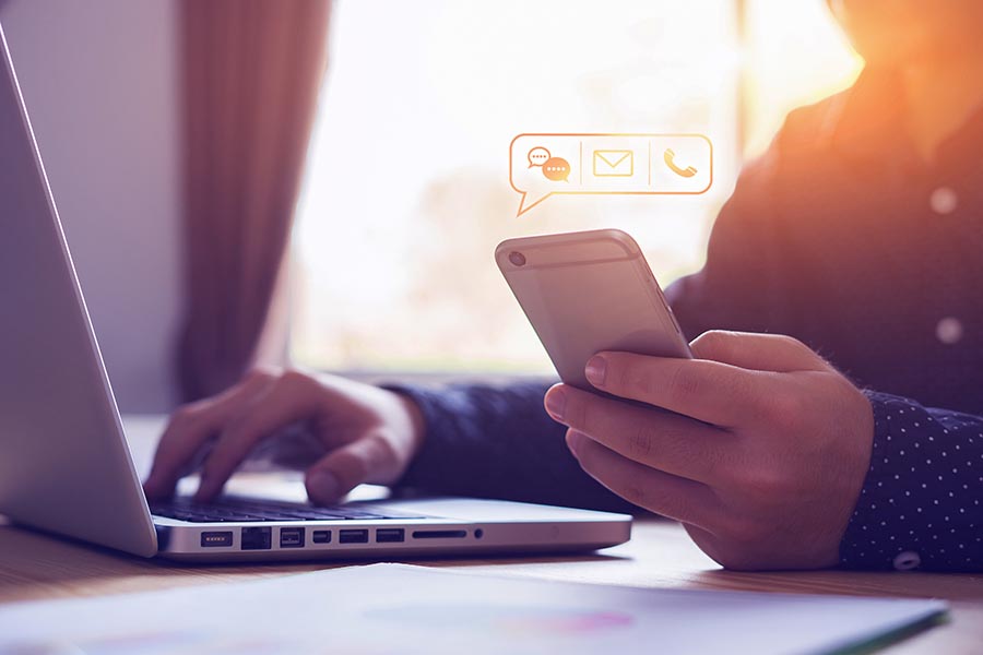 Contact Us - Person Using a Phone and Laptop, With Icons for Contact Options Hovering Over the Phone